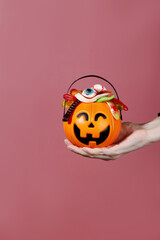 Trick or treat. Pumpkin Jack filled with various creepy sweets stands on stones and moss. Woman hand holds basket