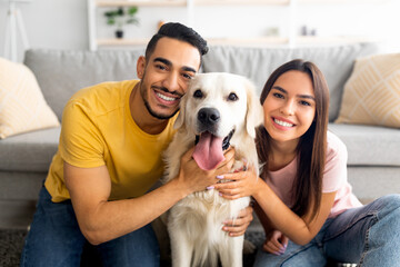 Portrait of smiling diverse couple hugging their pet dog, smiling at camera, indoors - Powered by Adobe
