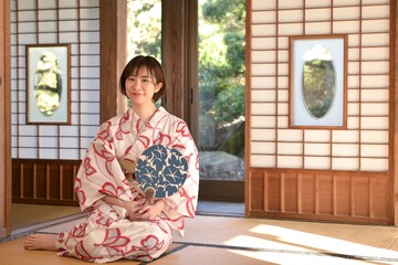 団扇を手に和室でくつろぐ若い浴衣姿の微笑む女性