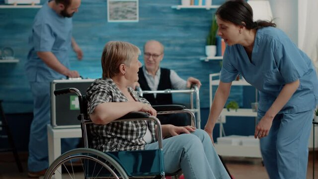 Disabled woman getting medical visit for checkup from nurse at nursing home facility. Retired patient with handicap sitting in wheelchair while talking to specialist about healthcare