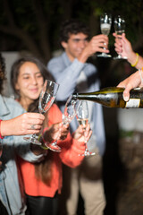 Close-up of champagne in glasses. Woman pouring beverage in glasses. People smiling at background. Party, celebration, nightlife concept