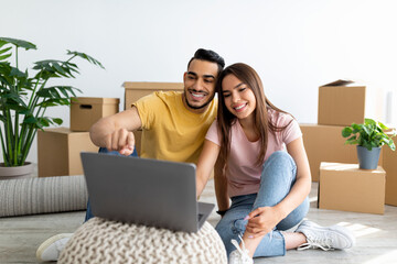 Cheerful diverse couple with laptop searching for household goods for their new home online, using...