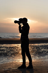 man photographer shoots on camera on the beach at sunset