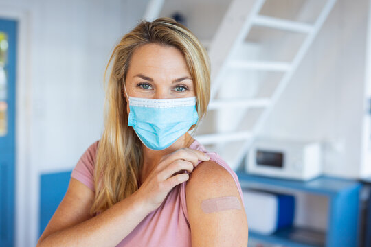 Caucasian woman wearing face mask showing plaster on arm where they were vaccinated