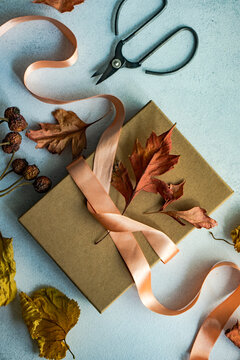 Autumnal gift box tied with a ribbon and dried autumn leaf decorations on a table