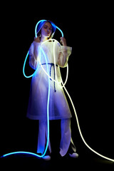 Stylish woman in transparent white raincoat and flexible blue and white neon tube lights