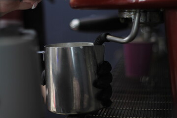 the hands of the barista whipping milk in the coffee machine