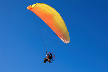 Yellow Powered Parachute, operated by pilot flies flies in the bright blue sky 