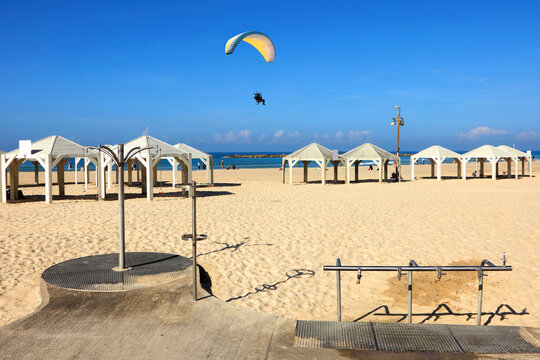 Calm sandy beach on sunny Mediterranean sea. Yellow Powered Parachute flies in blue sky along the shore. Wooden canopies, clean sand, showers. Tel Aviv beaches are popular recreation area in Israel