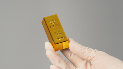 Gold bar in hand and wear latex glove isolated on grey background.