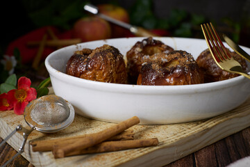 roasted red apples with cinnamon and honey in white earthenware dish on dark wooden table