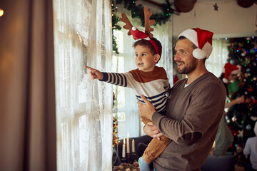 Happy father and son look through the window while being at home on Christmas.