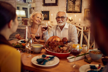 Happy senior man toasts to his family during Thanksgiving meal at dining table.