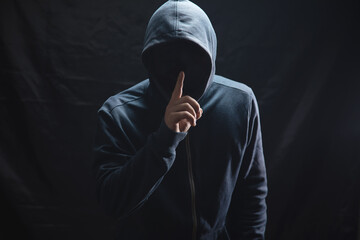 the hacker in the hood makes a silence gesture - obrazy, fototapety, plakaty
