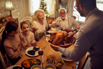 Close-up of man serves Thanksgiving turkey during family meal at dining table.