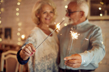 Close-up of mature couple has fun with sparklers on Christmas at home.