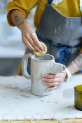 Relaxation of working with raw clay: closeup of young artist woman forming jug from ceramic material with water and sponge. Female craftswoman professional occupation or leisure entertainment hobby