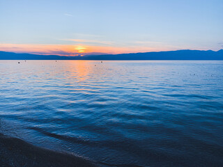Beautiful sunset on the lake, natural colors, silhouette of the mountains background, deep blue color