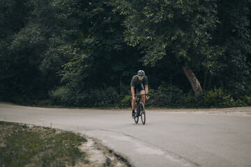 Athletic man in sport clothes cycling among green forest