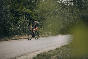 Fototapeta na wymiar Muscular sportsman riding bike on high speed among forest