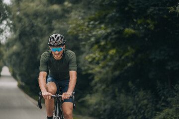 Healthy and fit man riding bike on road among green nature