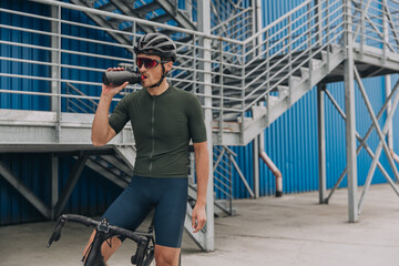 Tired cyclist drinking water after workout on city street