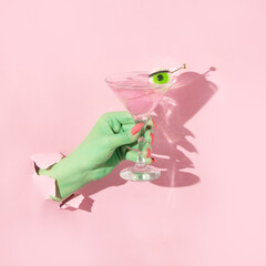 Halloween creative layout with green witch hand with bright pink nails holding martini cocktail...