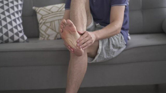 Foot pain, man suffering from feet ache in home interior and does self-massage, podiatry concept