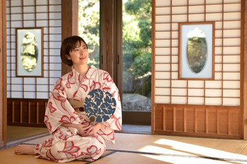 団扇を手に和室でくつろぐ若い浴衣姿の微笑む女性