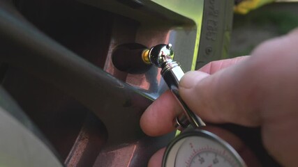 Closeup POV shot of a man’s hand removing the dust cap from a tire / tyre valve, then attaching a traditional manual needle gauge to take a pressure reading.