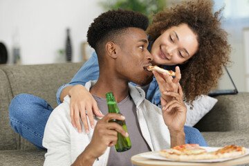 happy couple watching tv with a pizza and a beer