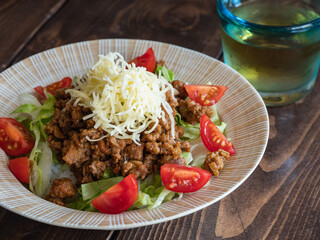 沖縄料理のタコライス。スパイシーに炒めた挽き肉とレタスとトマトとチーズをご飯のトッピングした料理。
