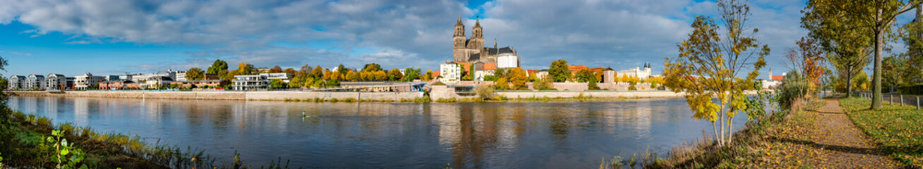 Panoramic view over Magdeburg historical downtown, Elbe river, city park and the ancient medieval cathedral in golden Autumn colors at blue cloudy sky and sunny day, Magdeburg, Germany. - obrazy, fototapety, plakaty