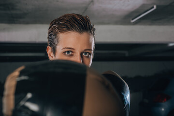 Closeup portrait of serious young female punching with gold boxing gloves