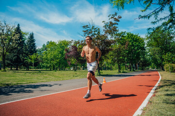 A strong attractive man running shirtless outside in the park