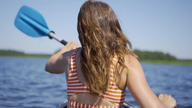 Beautiful young woman kayaking on lake. Girl rowing oars on a kayak on the river. Sports hike, water rafting in nature.