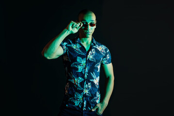 Fototapeta na wymiar Neon light studio close-up portrait of attractive male model in sunglasses and Hawaiian shirt. portrait photo of a dark-skinned handsome guy.
