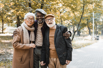 Happy multicultural men smiling at camera in autumn park