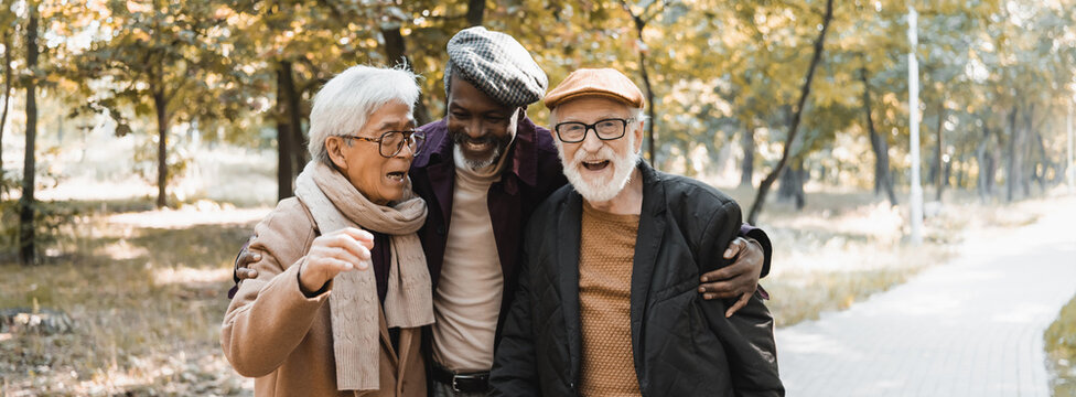 African american man hugging interracial senior friends in autumn park, banner