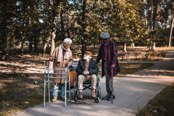 Multicultural friends with walking frame and wheelchair talking in autumn park