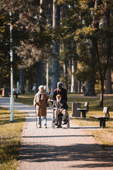 Fototapeta premium Multiethnic senior men with wheelchair and walking cane talking in autumn park