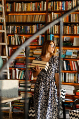 Back to school library concept. Student girl holding book on her hands on background of bookshelves in the library. Education and school concept.