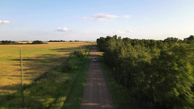 4k drone footage of car driving on red dirt road between lush green trees during sunset in the countryside of the USA.