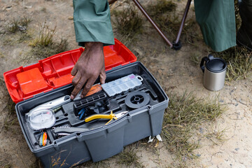 Cropped view of african american man taking tool from toolbox during fishing outdoors