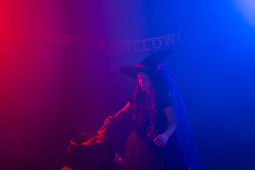 Child girl witch preparing a potion in the cauldron at halloween holidays. Copy space.