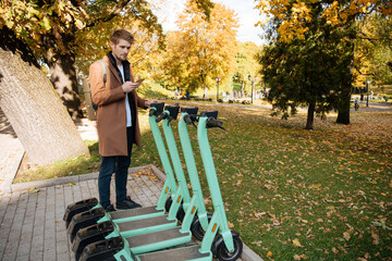 Transportation ecology. Green sustainable mobility Young man unlocks an e-scooter with his mobile phone. Electric scooter new way city. Green transportation. Sustainable climate neutral cities goals © Girts