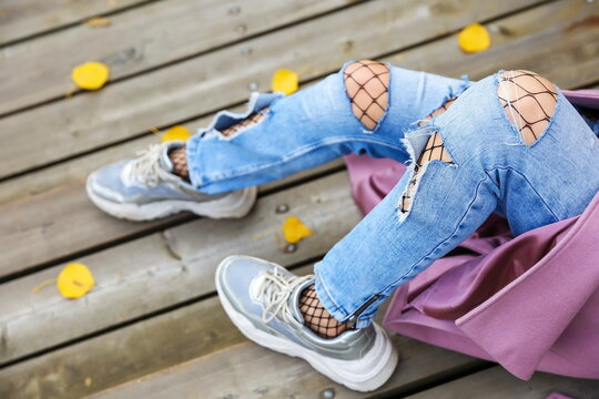 woman legs wearing ripped jeans and fishnet pantyhose close up. girl wearing torn jeans and fishnet tights close up outdoors. woman sitting on the stairs in autumn park