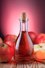 Bottle of apple cider and red apples on wooden background illuminated by red light. Soft focus.