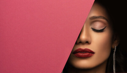 Face of a young beautiful girl with a bright make-up and with plump red lips peeks into a hole in...