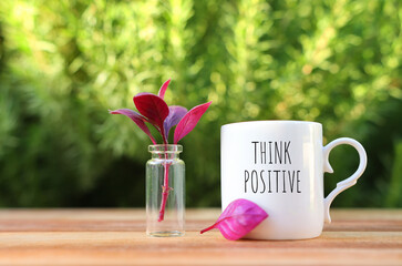 A cup of coffee on a wooden table in the garden with the text think positive